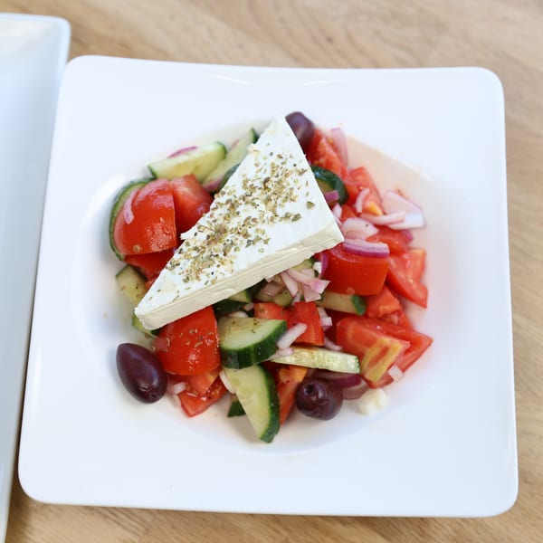 A fresh Greek salad with tomatoes, cucumbers, red onions, olives, and a large feta cheese block.