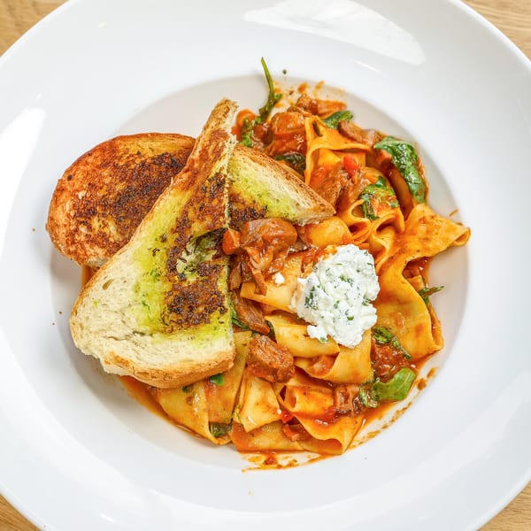 Pappardelle pasta with meat sauce, spinach, ricotta, and two slices of garlic bread.