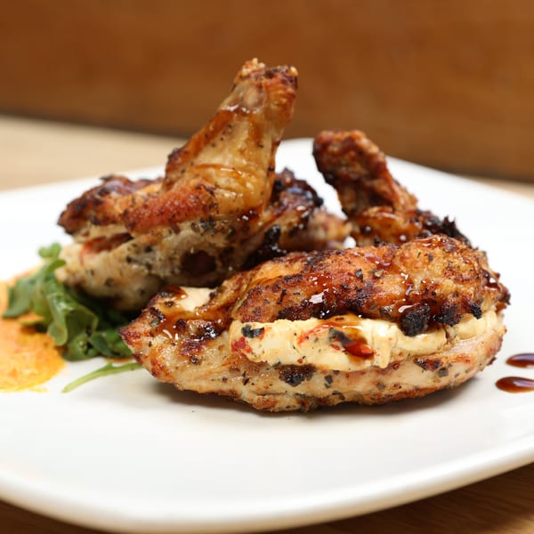 Grilled chicken wings and stuffed chicken breast with sauce and greens on a white plate.
