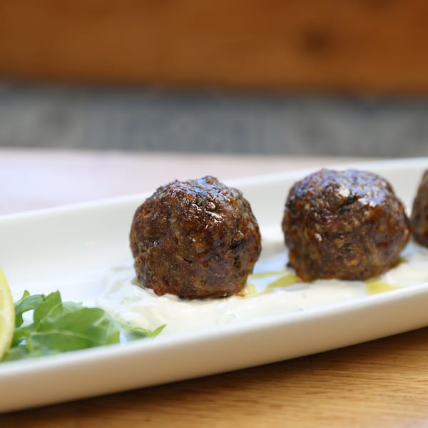 Three meatballs on a white plate with a dollop of sauce, a lemon wedge, and greens.