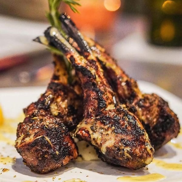 Grilled lamb chops with herbs and a creamy sauce, served on a white plate.