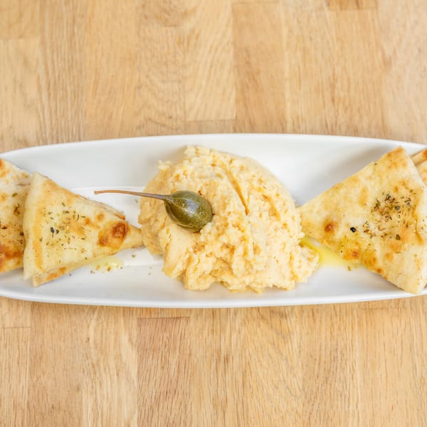 Hummus with a caper on top, served with pita bread triangles drizzled with olive oil.