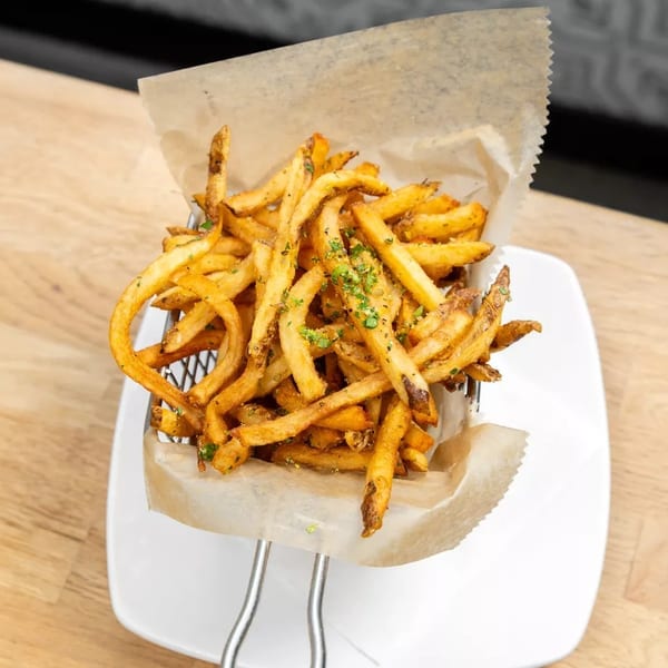 Crispy golden french fries seasoned with herbs, served in a metal basket lined with parchment paper.