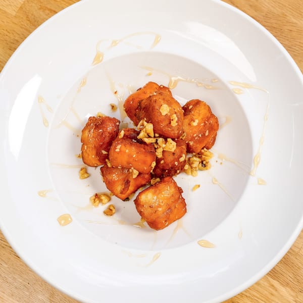 Golden-brown fried dough pastries drizzled with honey and sprinkled with chopped walnuts on a white plate.