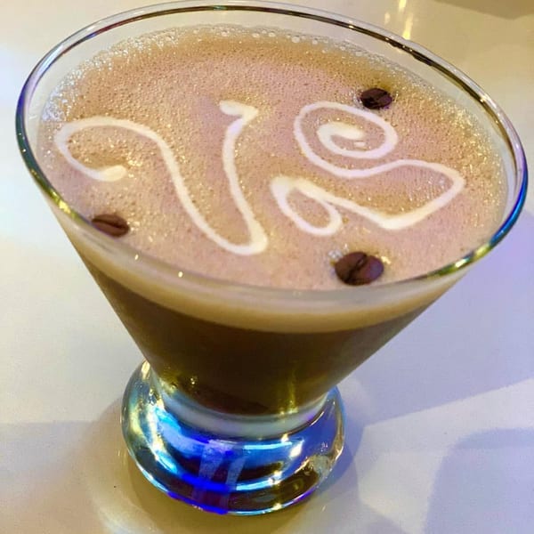 Espresso martini with foam art and coffee beans in a martini glass with a blue-lit base.