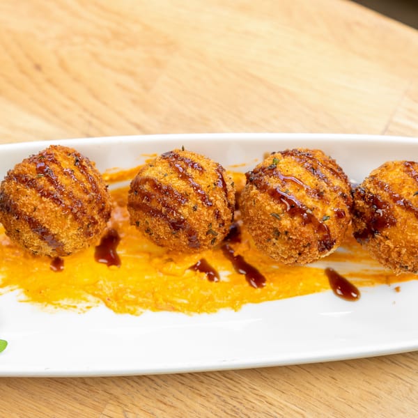 Four golden-brown arancini balls drizzled with dark sauce, served on orange puree with arugula.