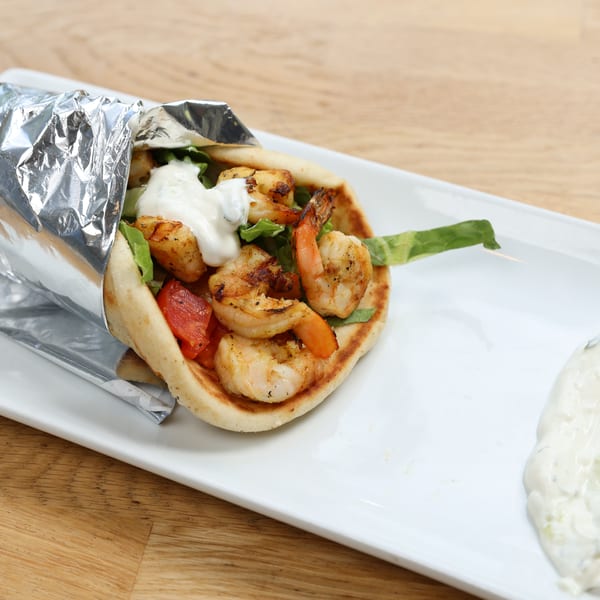 Shrimp pita wrap with lettuce, tomatoes, and tzatziki sauce, served on a white plate.