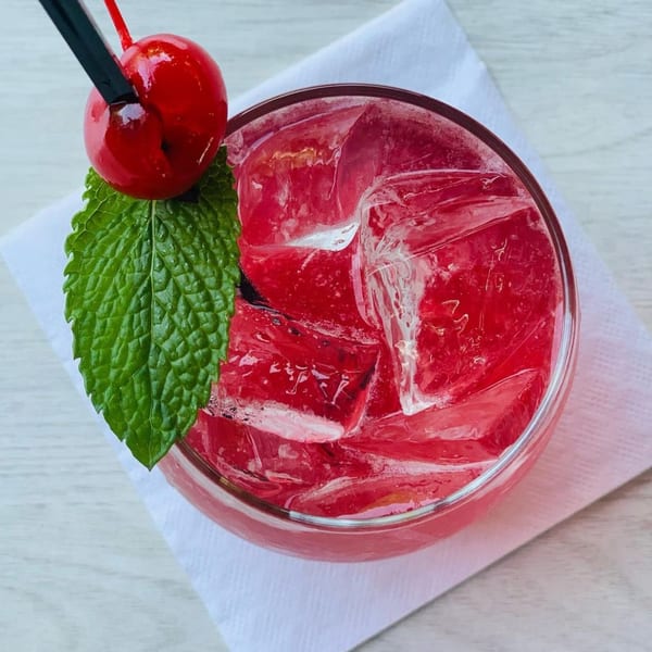 Top-down view of a vibrant red cocktail with ice, garnished with a cherry and mint leaf.