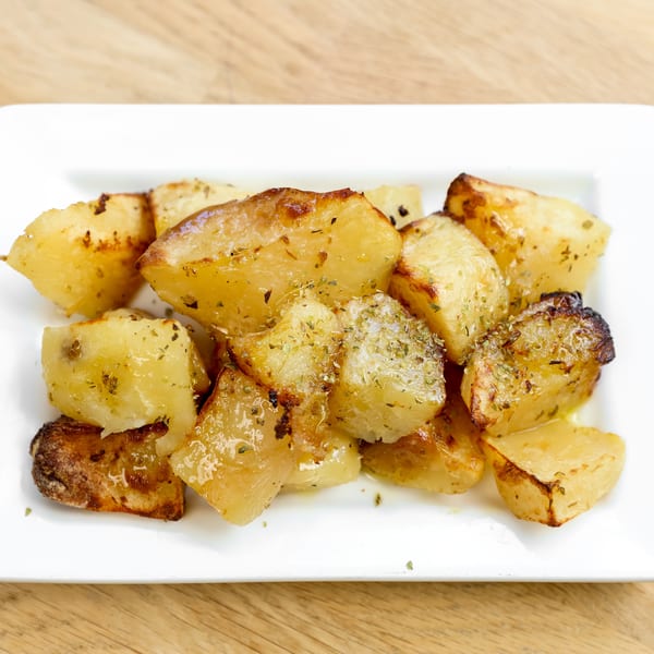 Golden roasted potatoes seasoned with herbs, served on a white rectangular plate.